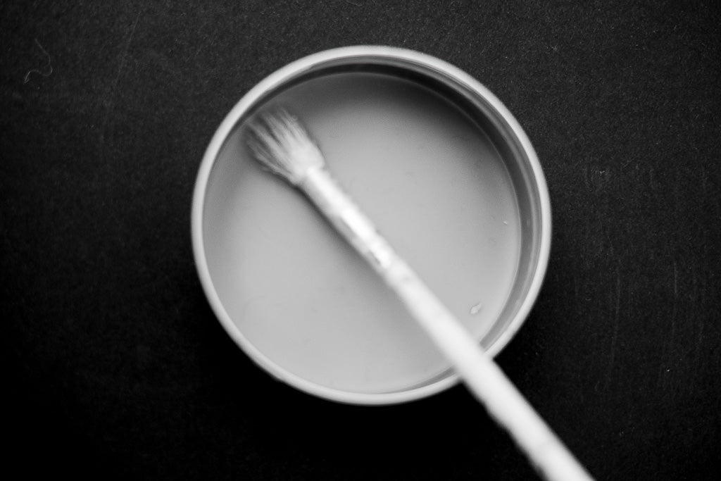 BW photograph in studio of wax in tin with paintbrush on black paper. 