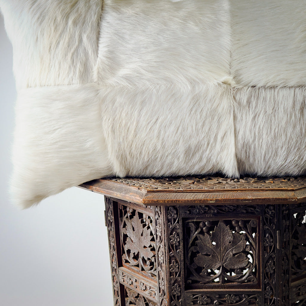 Quilted hair on hide lumbar pillow in light gray sitting on ornate stool.  