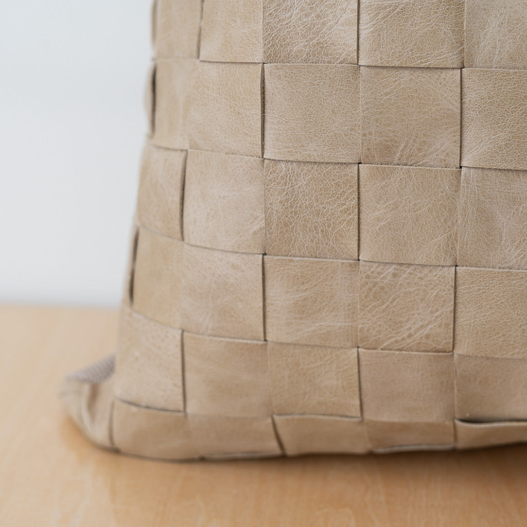 Tan leather woven pillow on neutral board and background. 